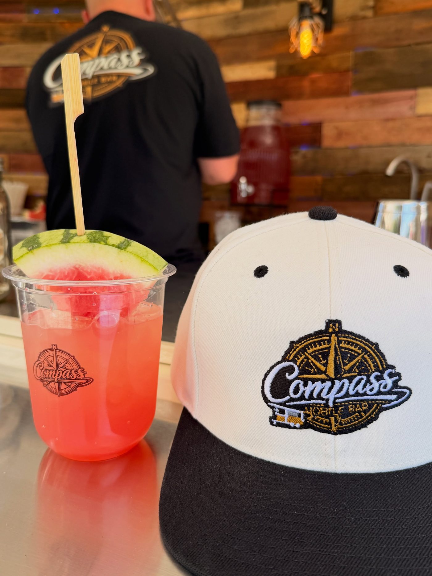 Watermelon cocktail in a branded cup next to a Compass hat
